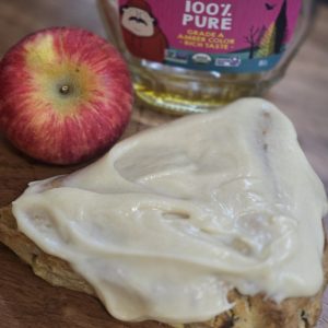 Glazed apple cinnamon scone beside an apple and maple syrup